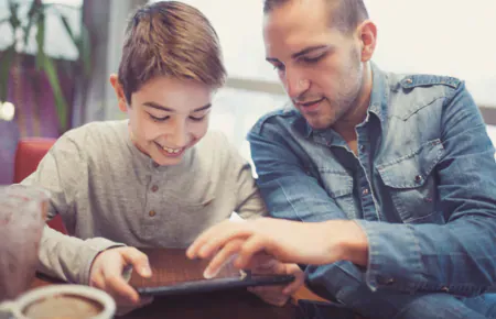 Smiling child shares digital tablet activity with interested father