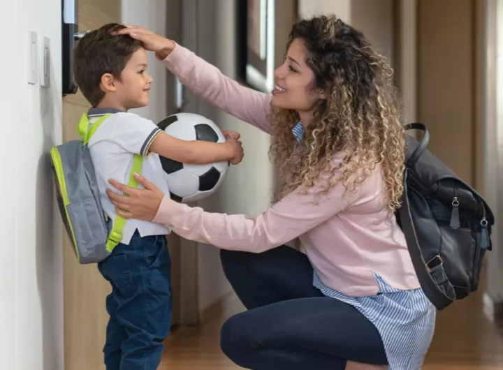 A mom saying goodbye to her son before the childcare or school drop-off,  giving him a pat on the head while he holds a soccer ball