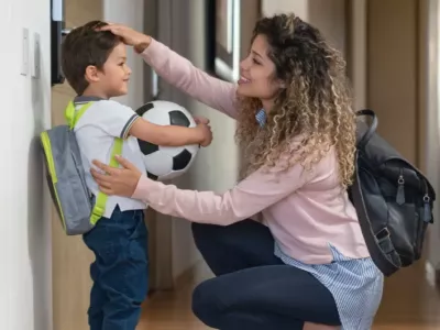 A mom saying goodbye to her son before the childcare or school drop-off,  giving him a pat on the head while he holds a soccer ball