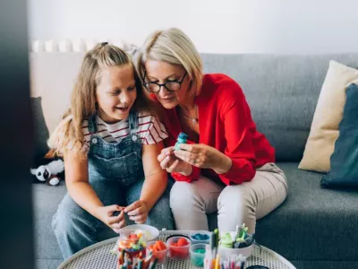 A grandmother and her granddaughter sitting on the couch, enjoying arts and crafts together at a table.