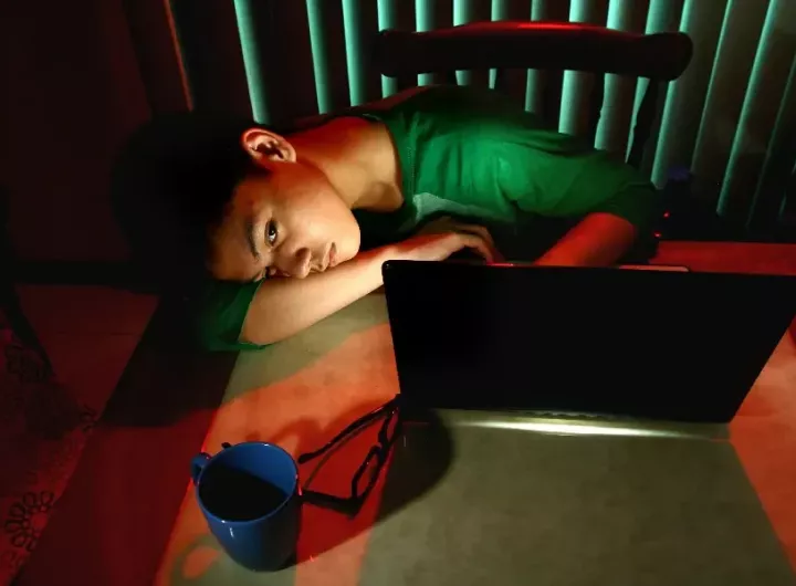 teenage boy lying slumped in front of computer at night